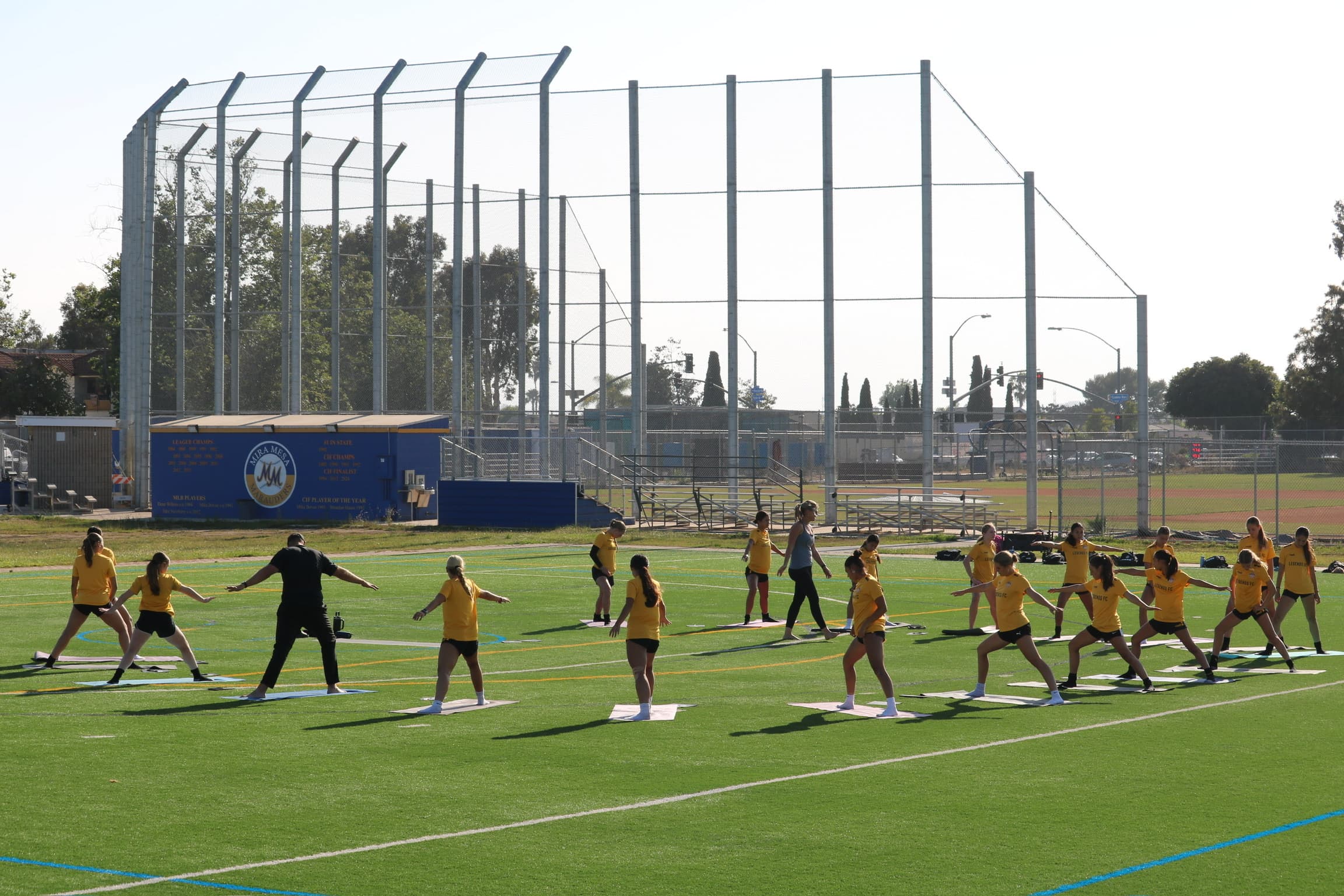 Girls holding warrior pose with a coach during a Mind Body Athletes field session